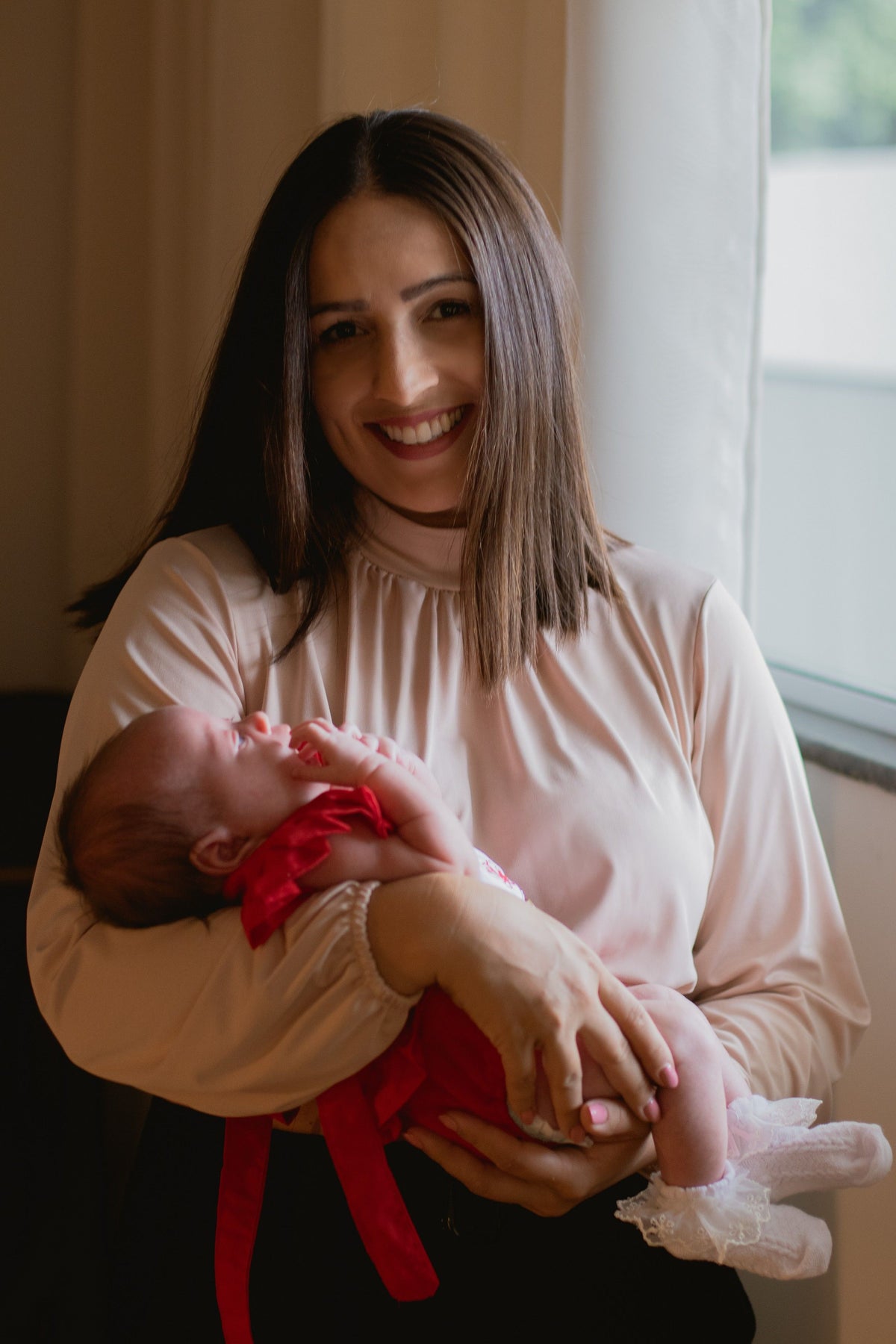 A mother tenderly holding her newborn baby close indoors, captured in warm, soft natural light.