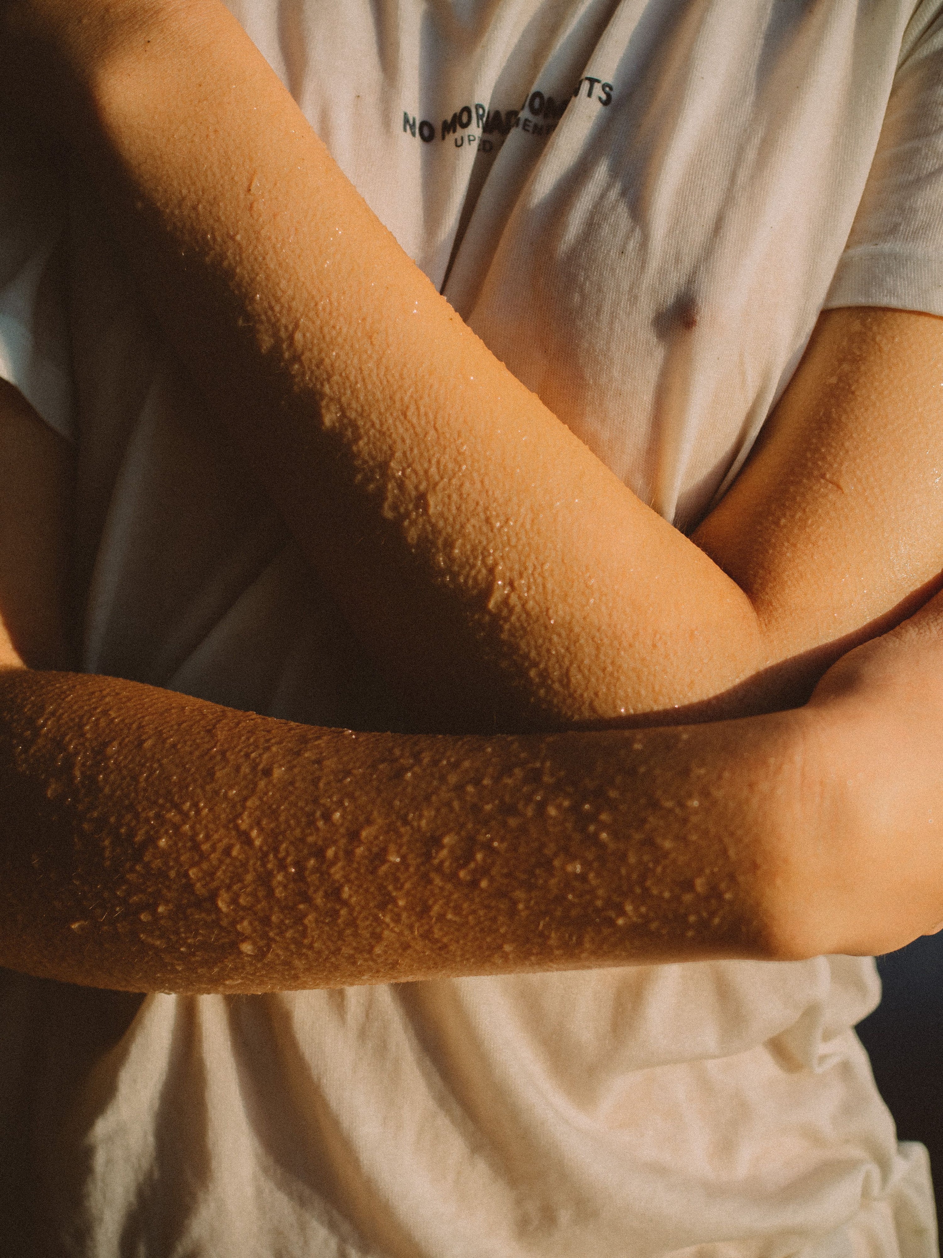 Close-up of bare arms and hands with water droplets on the skin, lit in warm golden light, evoking a healthy skin barrier holding on to moisture.