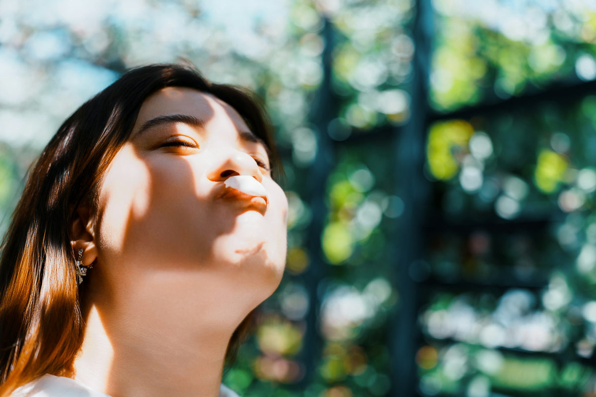 Close-up of a woman's face tilted toward warm sunlight with her eyes gently closed, showing the soft skin around her eyes